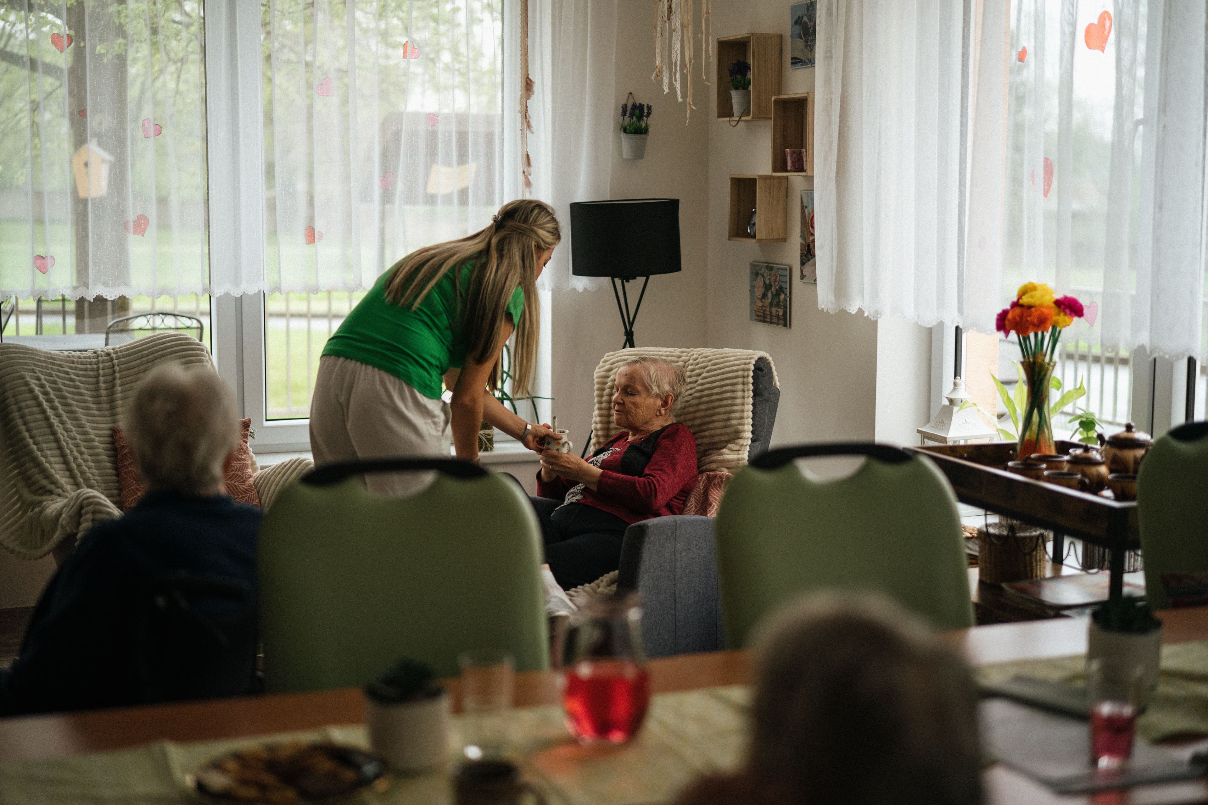 Caregiver serving tea to a resident in a cozy facility common room